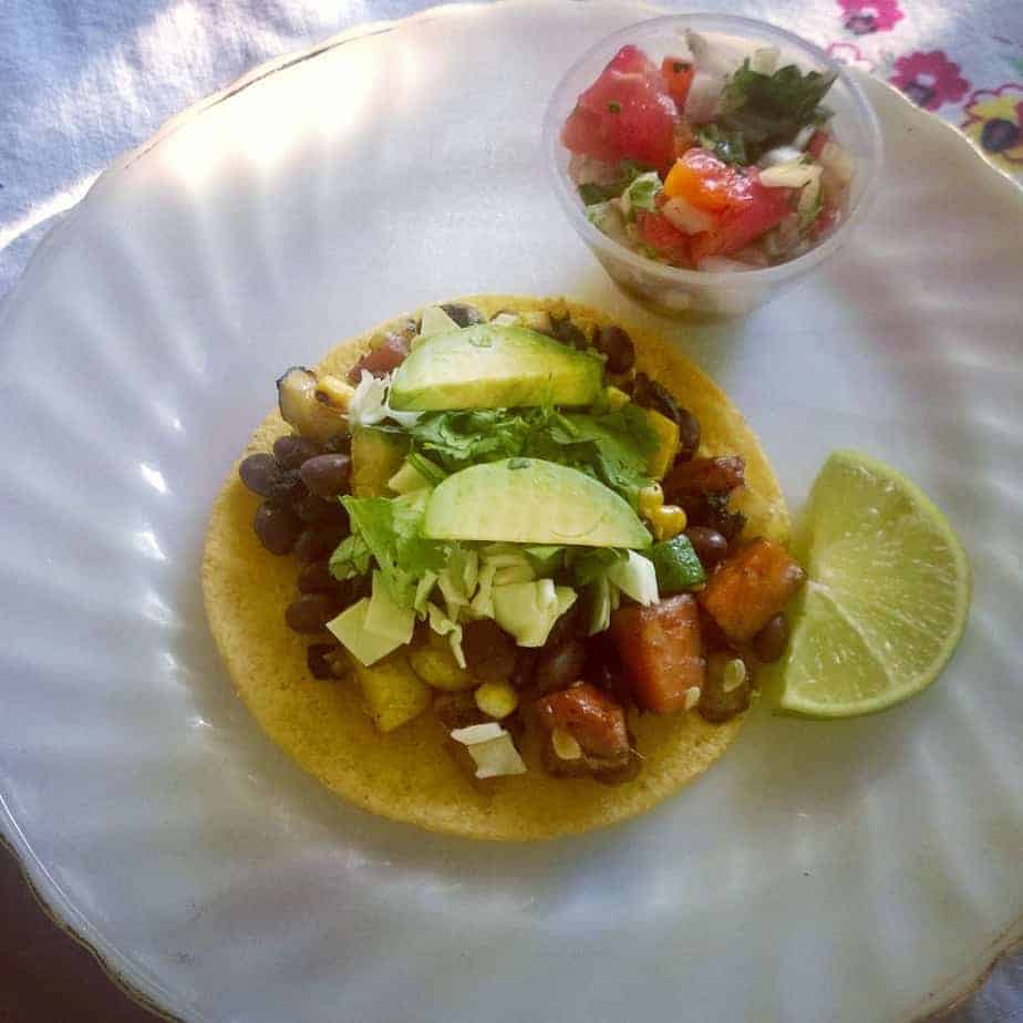 Black bean and corn tostado that includes roasted vegetables and topped with an avocado